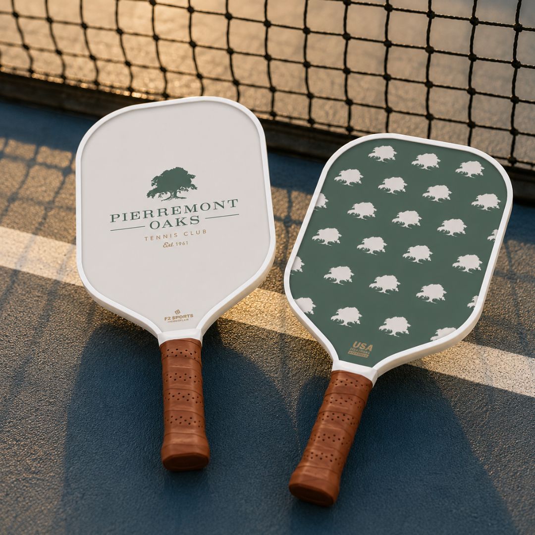 two pickleball paddles from pierremont oaks tennis club laying on court by net
